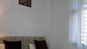A neatly made bed with white and dark pillows, a headboard, and a painting on the wall. - Yogamu India (Rishikesh)