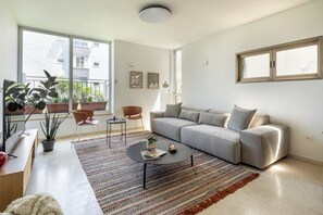 Un salon moderne avec un canapé gris, une table basse et une grande fenêtre donnant sur des immeubles.