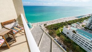 A balcony with a wooden chair and a view of a beach and resort area. - Beachfront Paradise - Spectacular Ocean Views - Great Location & Amenities! (Sunny Isles Beach)