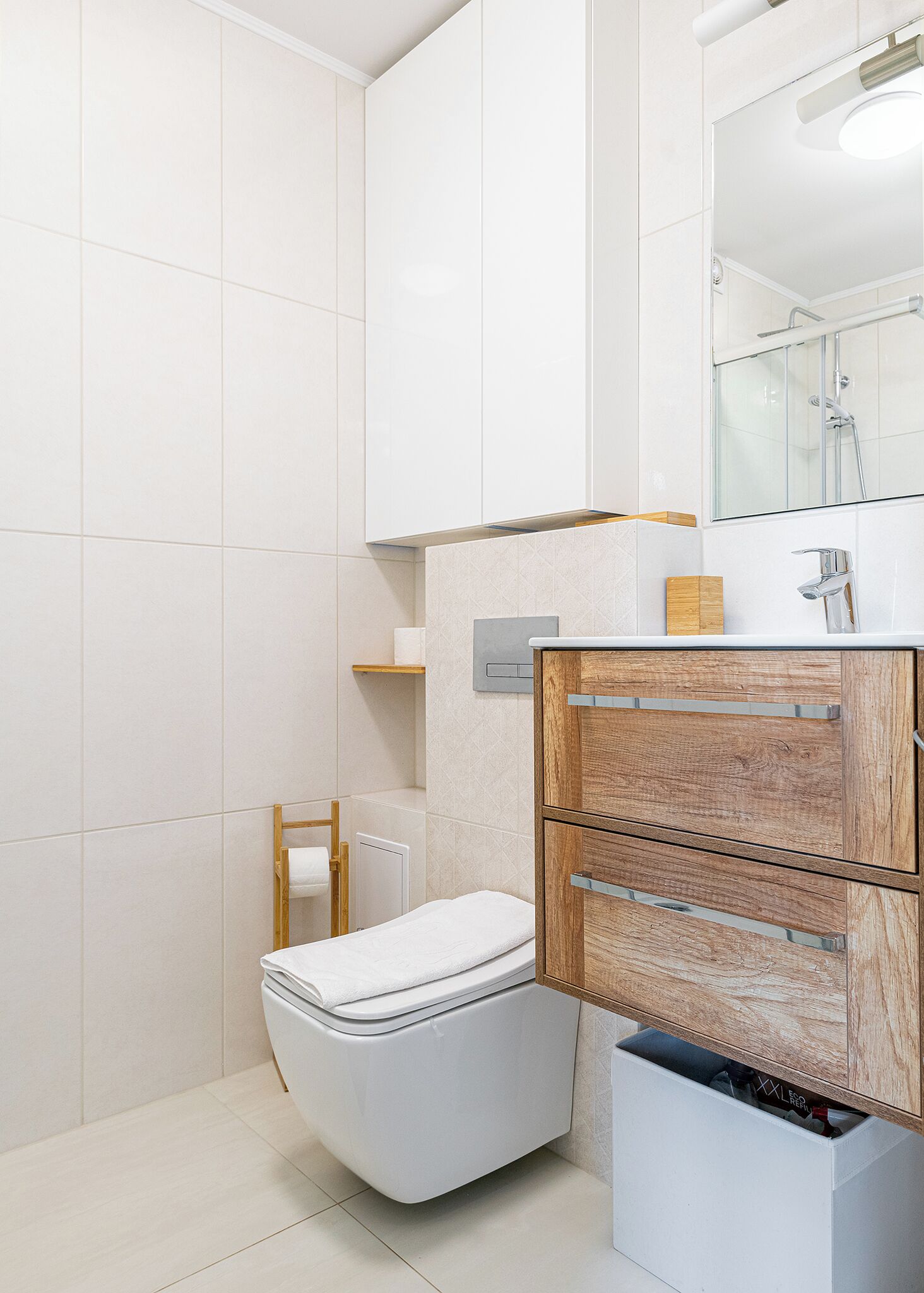 Ein modernes Badezimmer mit weißen Fliesen, einem Holzwaschtisch, einer Toilette und einer Duschkabine aus Glas.