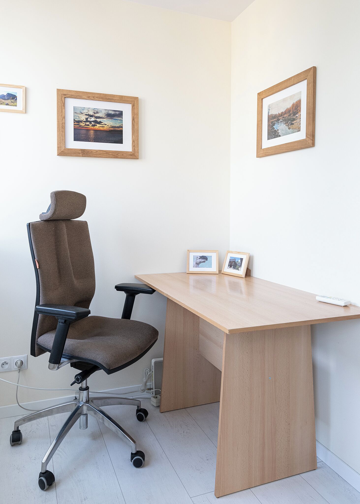 Un espace de bureau moderne avec un bureau en bois, un fauteuil de bureau à haut dossier et deux photographies encadrées accrochées au mur.