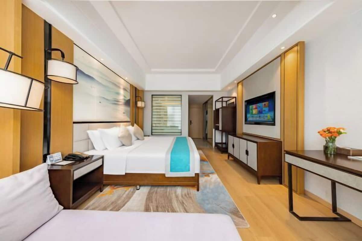 A modern hotel room with a bed, bedside table, TV, and a desk with a chair.
