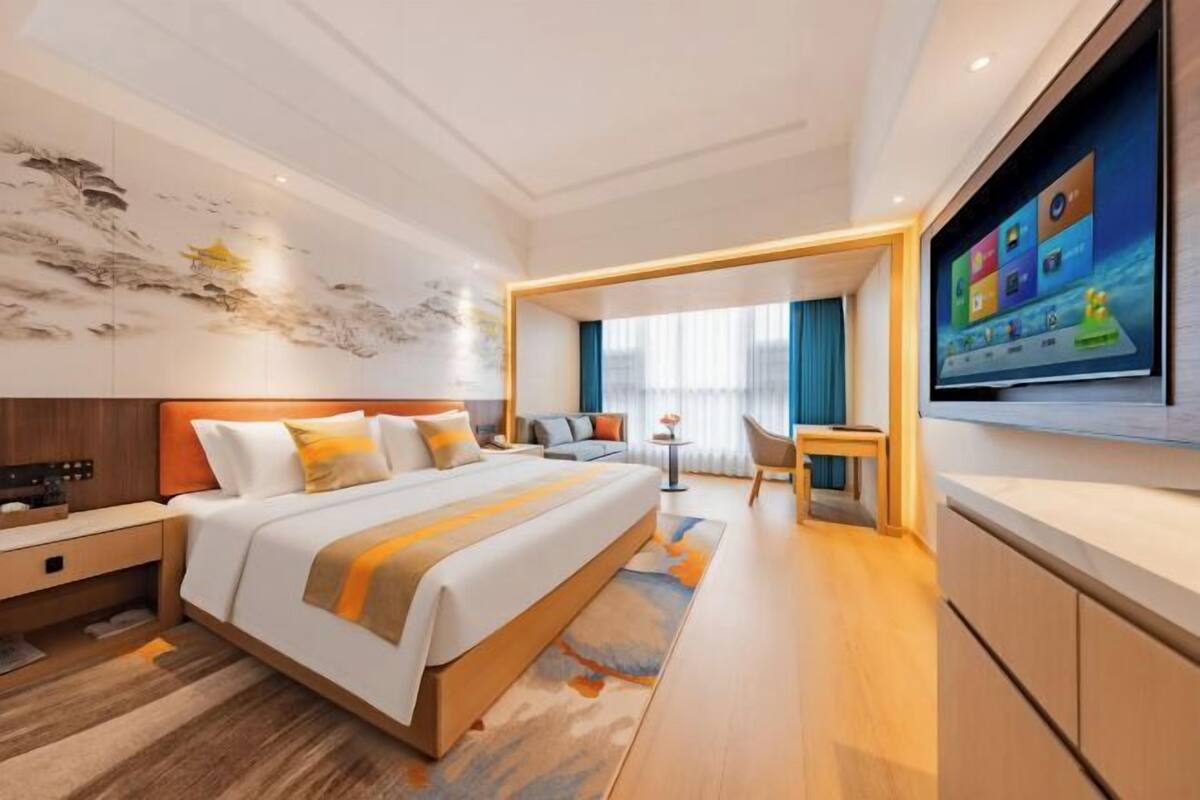 A modern hotel room with a large bed, a television, a desk, and a view of the city.