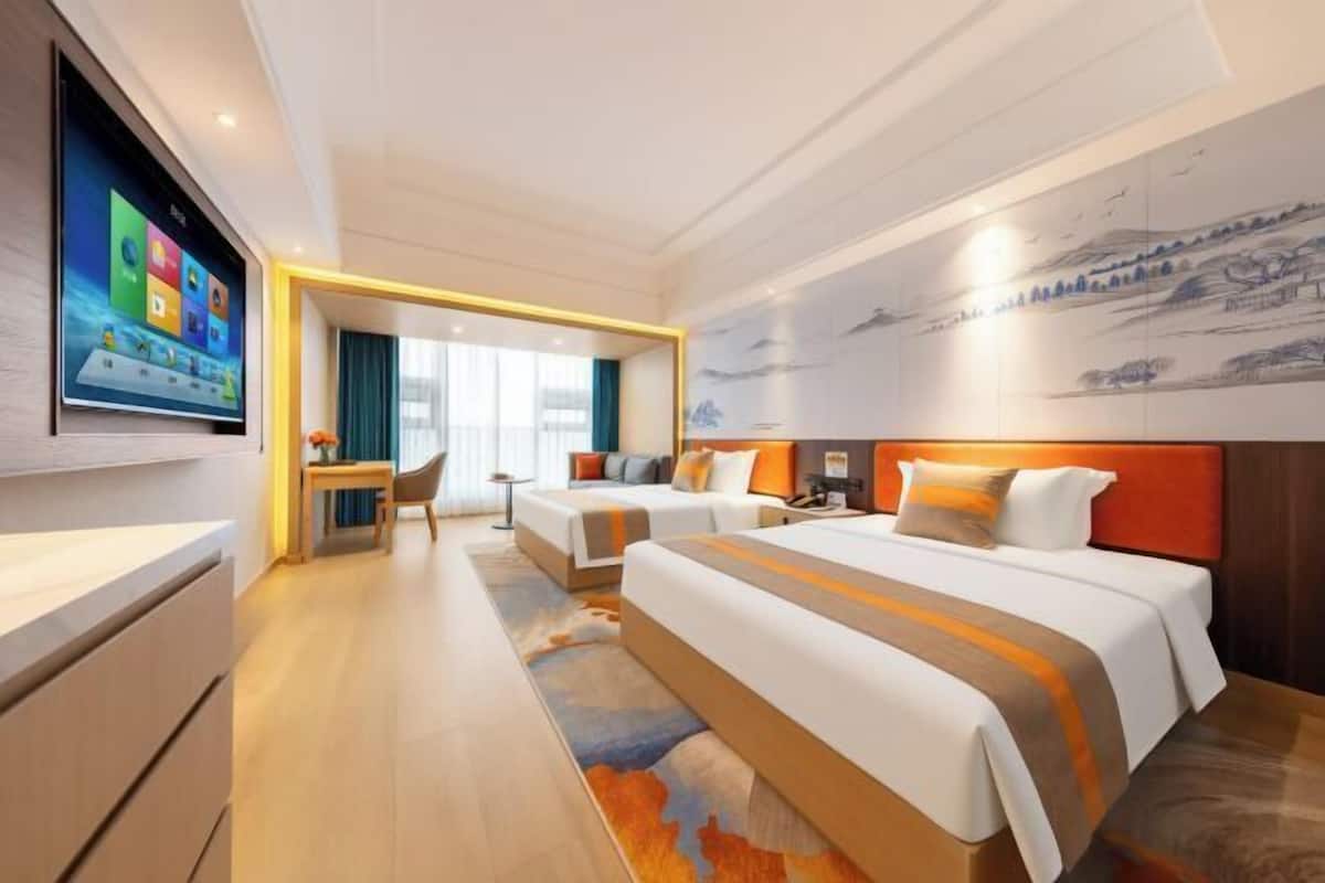 A hotel room with a large bed, a desk, a television, and a mural on the wall.