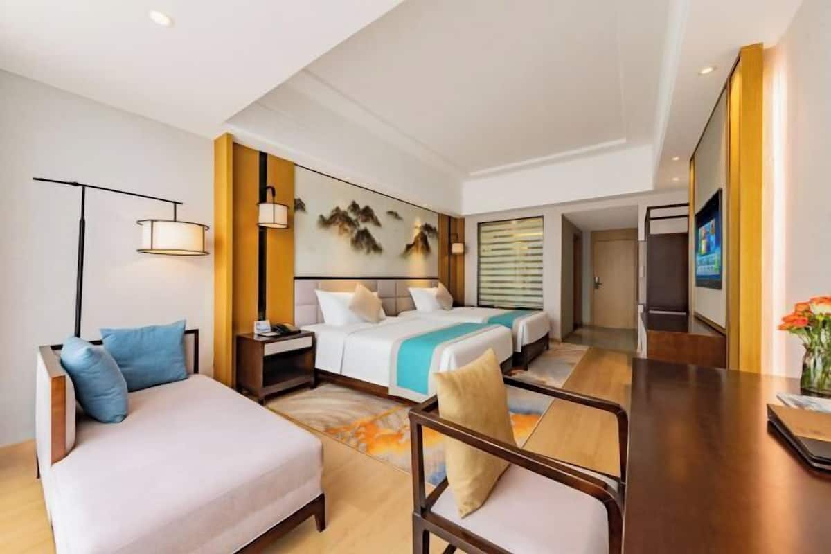 A hotel room with a bed, a desk, a chair, a sofa, and a TV.