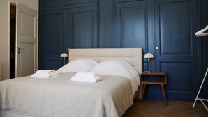Een net opgemaakt bed met twee gevouwen handdoeken, een nachtkastje met een lamp en een houten vloer.