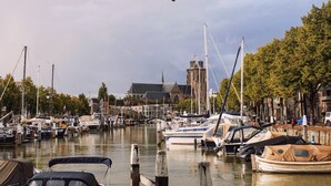 Een jachthaven met aangemeerde boten, een kerk op de achtergrond en een rij bomen langs de waterlijn.