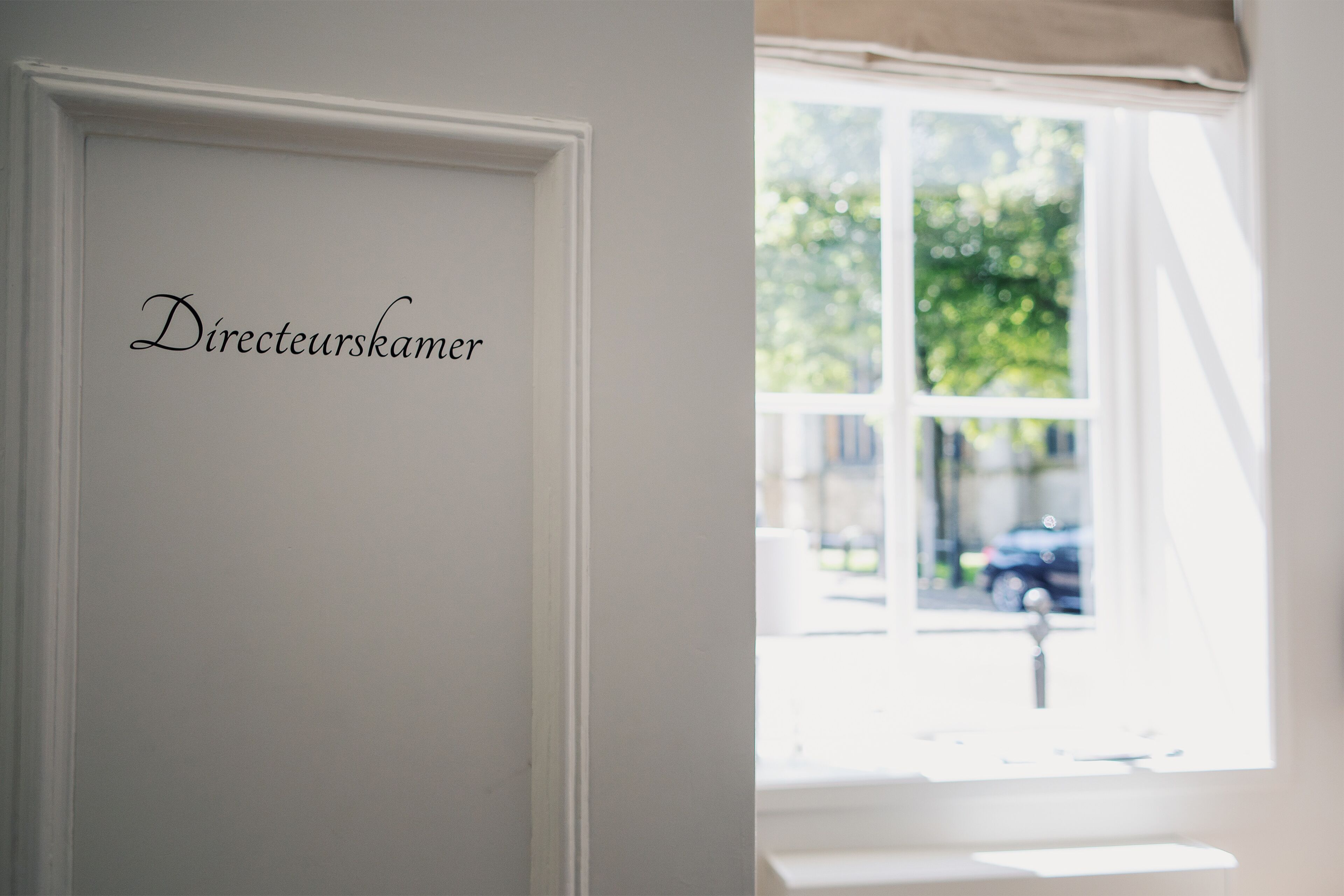 A room with a white door labeled "Directeurskamer" and a window with a view of the street outside.