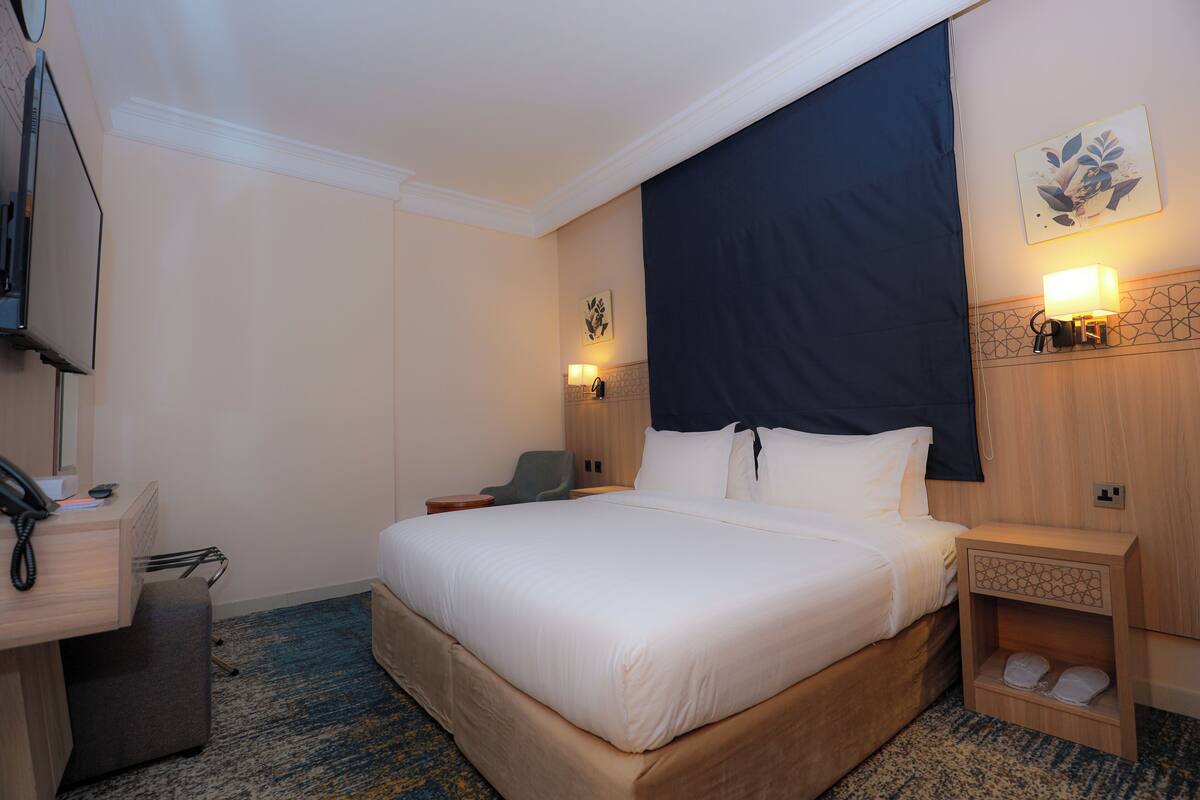 Una habitación de hotel con una cama grande, mesitas de noche, un escritorio con teléfono y una silla.