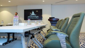 A conference room with a long table, multiple chairs, water bottles, and a presentation screen displaying hotel branding.