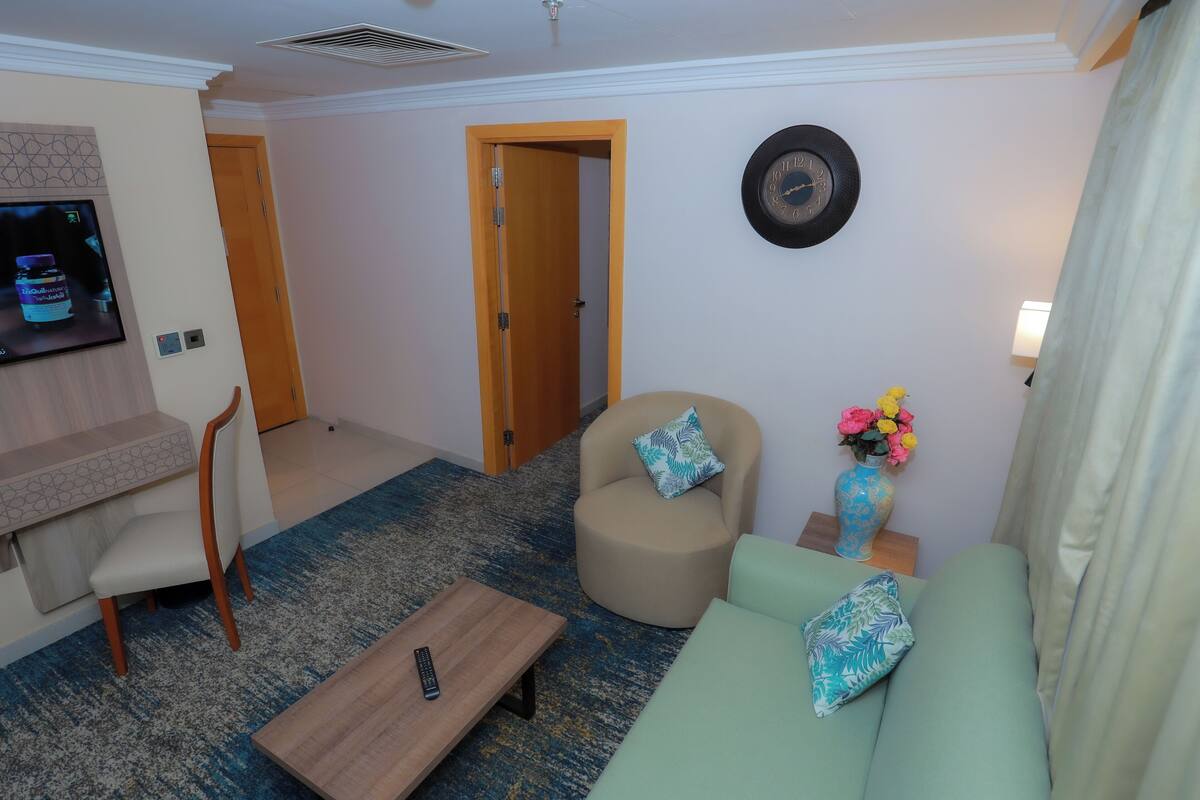 Una sala de estar con sofá, sillón, mesa de centro, televisor y un reloj en la pared.