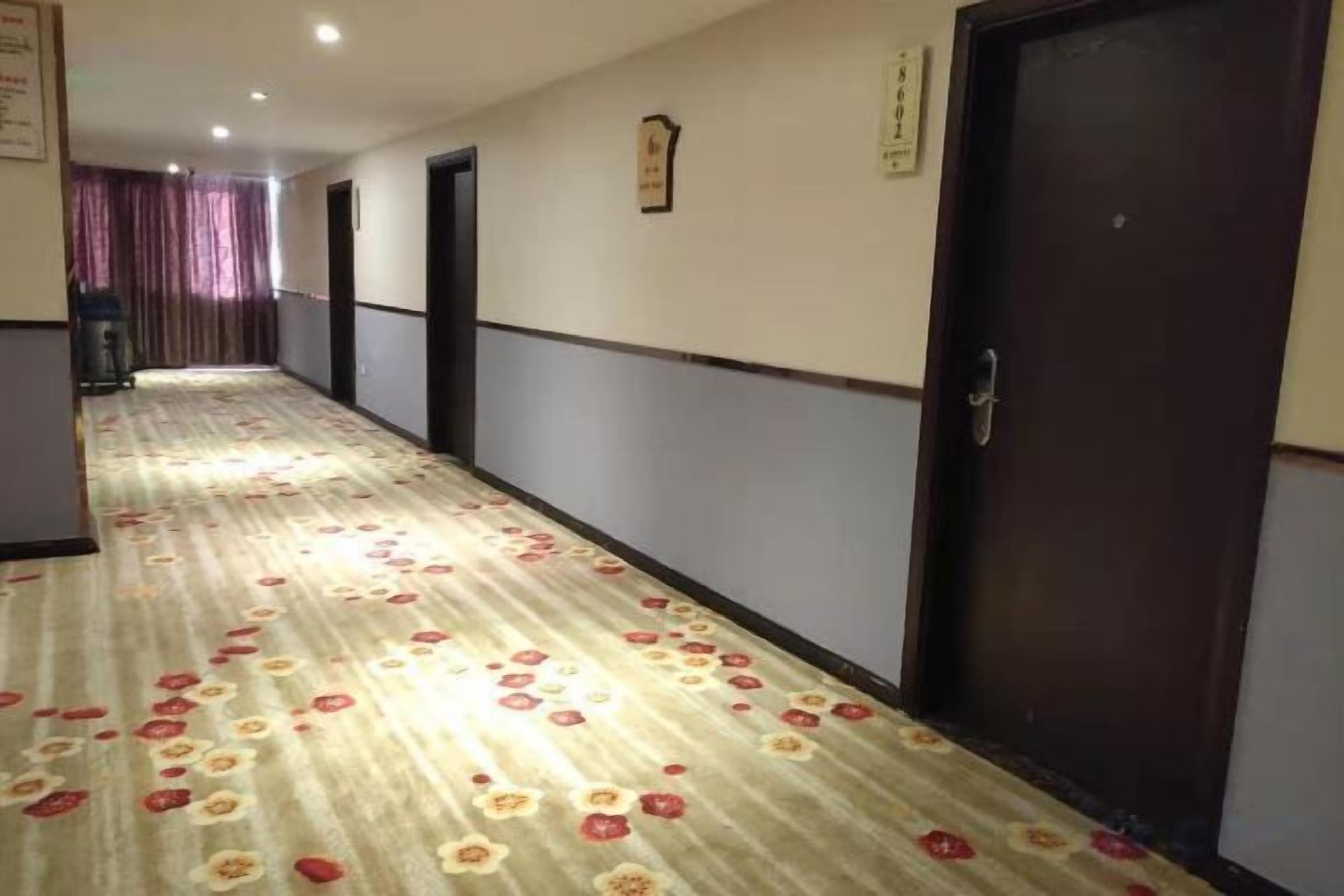 Un couloir d'hôtel avec un revêtement de sol en moquette, des portes et un comptoir d'accueil situé au fond.