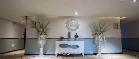 A reception area with a blue console, two tall vases with plants, and a decorative mirror on the wall.