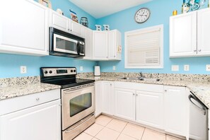 A kitchen with white cabinets, a stainless steel stove, a microwave, and a clock on the wall.