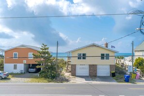 A two-story residential building with a garage, a small driveway, and a view of the ocean. - Barefoot Bumblebee - 2nd Row 5BR Home - Ocean Views from Decks and Porches (Surf City)