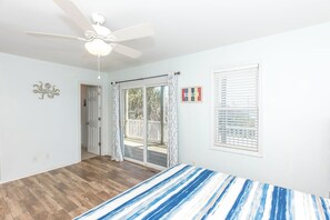 A bedroom with a bed, a ceiling fan, a window with blinds, and a door leading to a balcony. - Barefoot Bumblebee - 2nd Row 5BR Home - Ocean Views from Decks and Porches (Surf City)