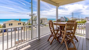 Een houten terras met een tafel en stoelen, met uitzicht op een strand en de oceaan.