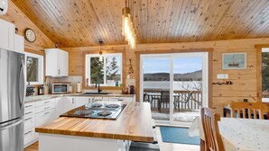 A cabin-style kitchen with a central island, wooden ceiling, and large windows overlooking a lake.