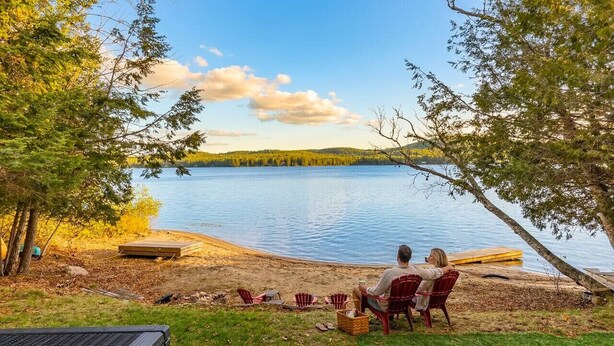 A lakeside view with chairs and a table under a covered area.