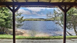 A covered outdoor area with a view of a lake, surrounded by trees.