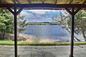 A covered outdoor area with a view of a lake and surrounding trees.