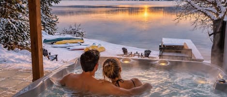 Una pareja en un jacuzzi con vistas a un lago y un paisaje nevado.