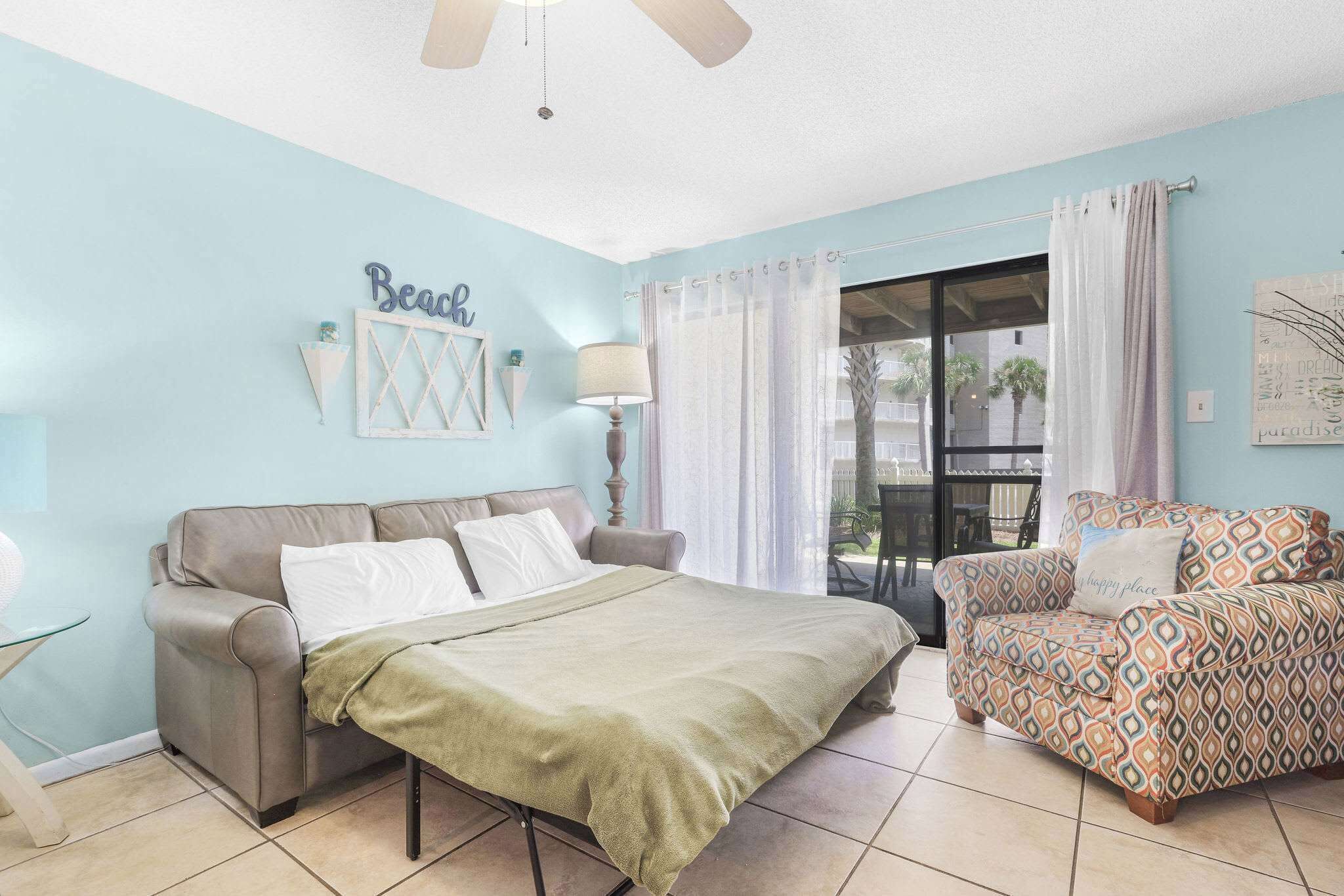 A bedroom with a bed, a sofa, a ceiling fan, and a view of the outdoors.