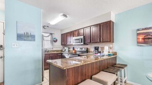 A kitchen with a central island, dark wood cabinets, a microwave, and a sink. - Seaside Beach 2102- Beachside! Ground floor (Orange Beach)