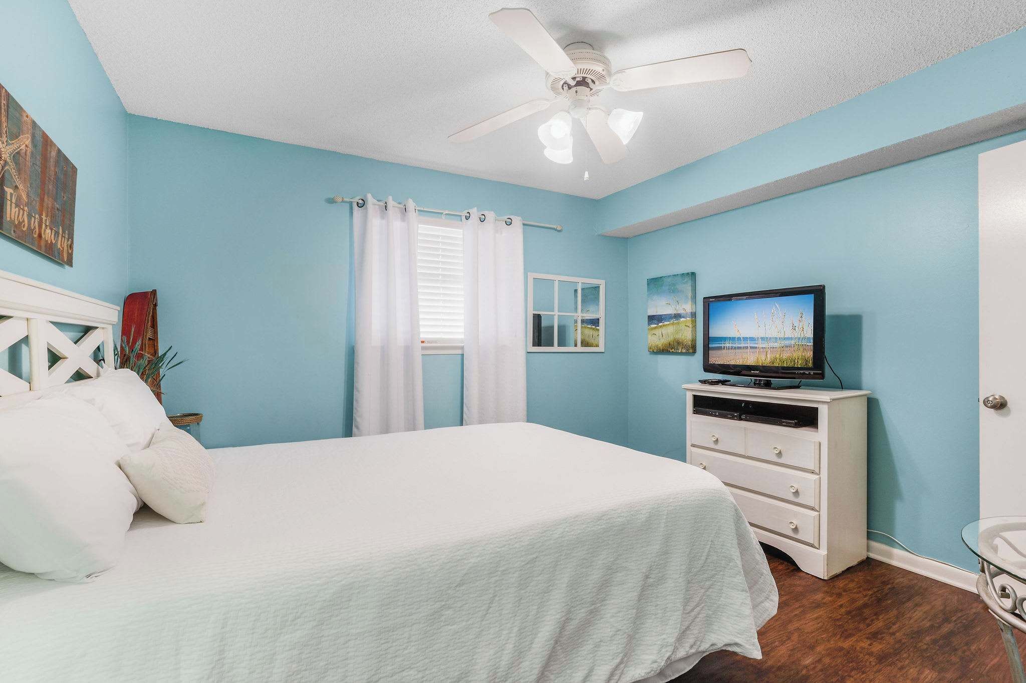 A bedroom with a bed, a television on a dresser, and a ceiling fan.