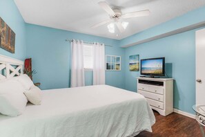 Une chambre à coucher avec un lit, un téléviseur posé sur une commode et un ventilateur de plafond.