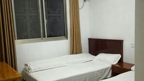 Ein Zimmer mit zwei Einzelbetten, einem Holztisch, einem Fenster mit Vorhängen und einem Holzkopfende.