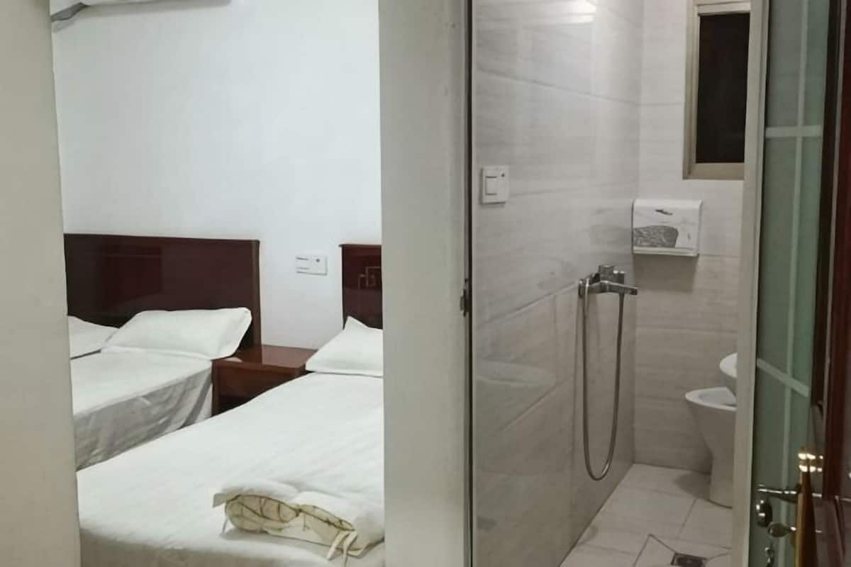 Hotellihuone, jossa on kaksi sänkyä, suihku ja wc.