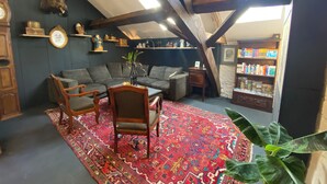 Un acogedor loft con pared azul oscuro, vigas de madera a la vista, un amplio sofá modular, una mesa de centro de madera, una alfombra estampada y una estantería llena de libros.