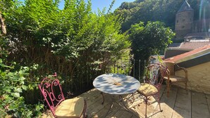 Un patio al aire libre con una mesa redonda y dos sillas, rodeado de abundante vegetación y un muro de piedra.