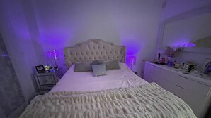 Un dormitorio con cabecera capitonada, un edredón grande y mullido, y dos lámparas de noche.