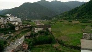 Un pueblo rural con edificios tradicionales, campos en terrazas y montañas al fondo.