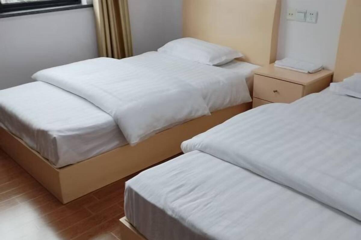 A hotel room with two single beds, a wooden nightstand, a small drawer, and a window with curtains.