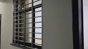Una ventana con diseño de celosía metálica, un marco oscuro y una pared blanca.
