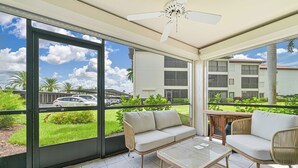 A sunlit patio with a sofa, chairs, and a table, overlooking a grassy area and a building with multiple windows. - First floor Cinnamon Cove Condo - Close to SWFL Beaches! (Fort Myers)