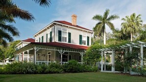 A two-story house with a red roof and green shutters, surrounded by lush greenery and palm trees. - First floor Cinnamon Cove Condo - Close to SWFL Beaches! (Fort Myers)
