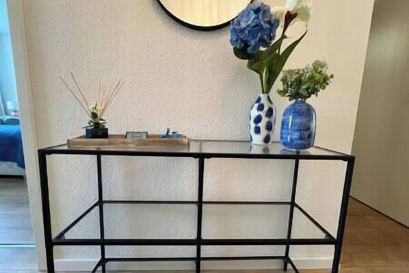 A black metal console table with a glass top, decorated with a blue vase and a white vase with blue patterns, and a small plant.