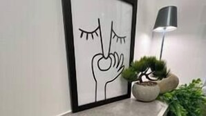 Une œuvre d’art encadrée représentant une main tenant une fleur, une plante en pot et une lampe posée sur un comptoir.