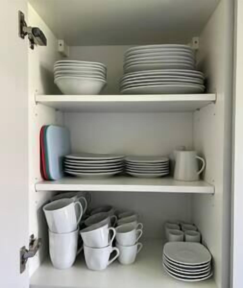A kitchen cabinet with multiple shelves holding plates, bowls, and cups.