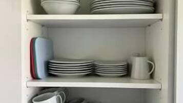 A kitchen cabinet with multiple shelves holding plates, bowls, and cups.