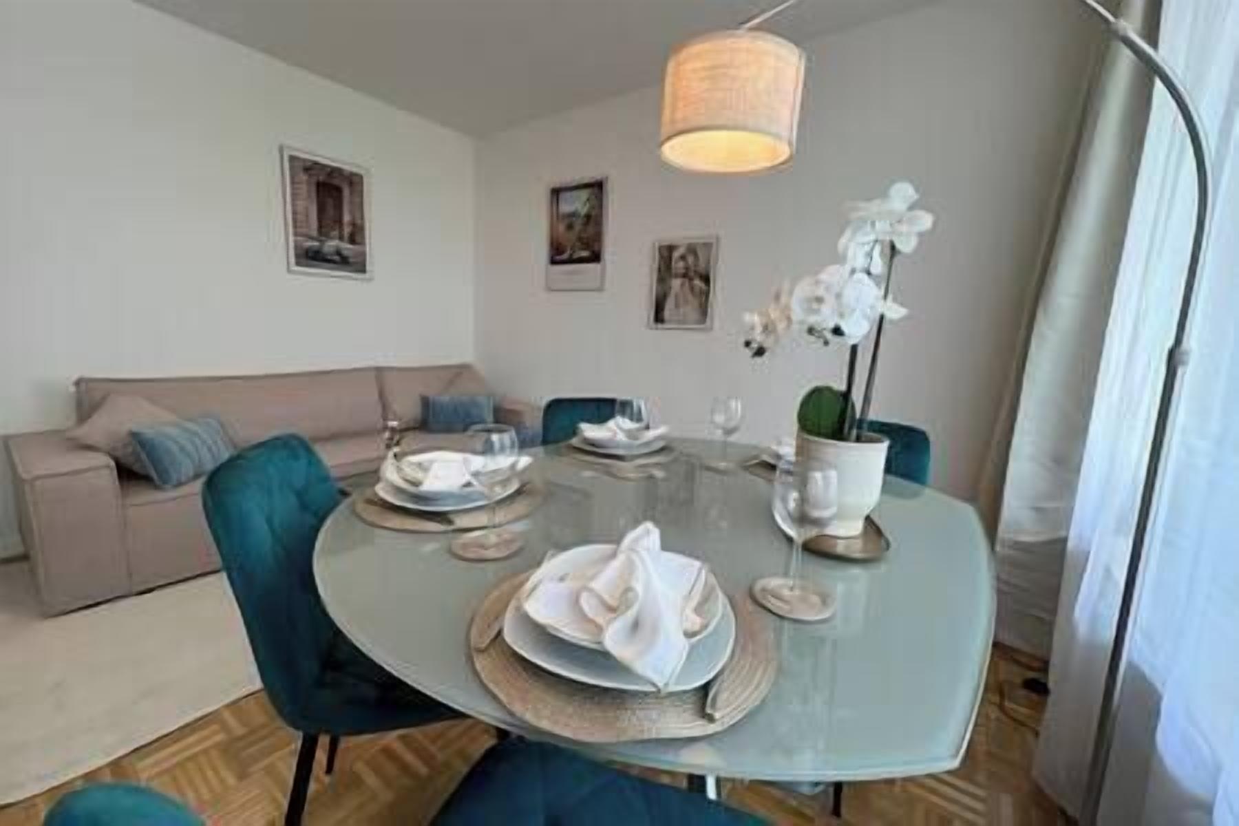 Een eethoek met een ronde glazen tafel, blauwe stoelen en een hangende lamp.
