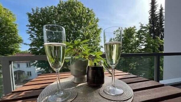 Deux verres de vin blanc sur une table en bois, accompagnés d’un set de table en fibres tressées, d’une plante en pot et d’un récipient en métal.