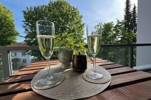 Two glasses of white wine on a wooden table with a woven placemat, a potted plant, and a metal container.