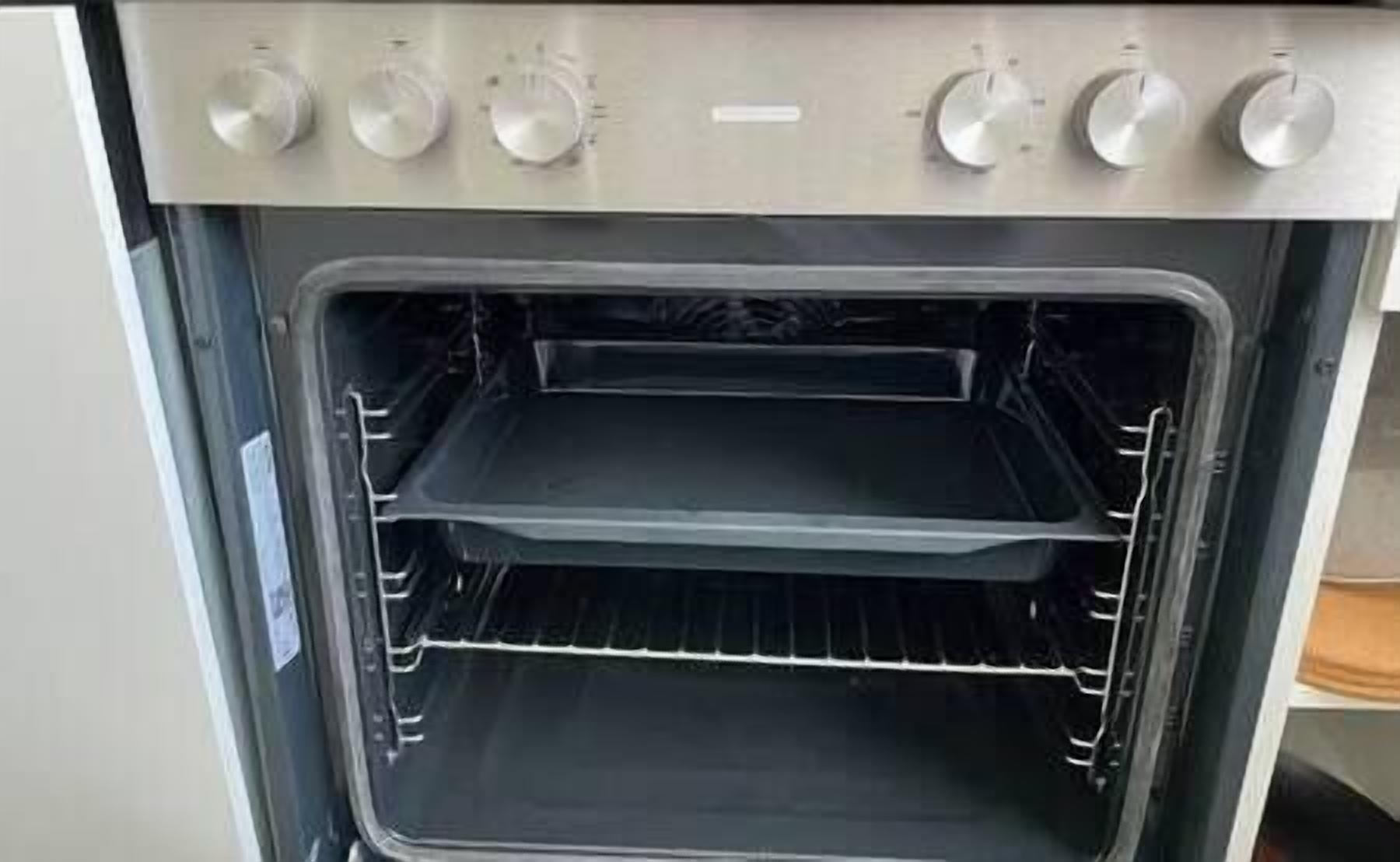An empty stainless steel oven with two racks and a control panel with knobs.