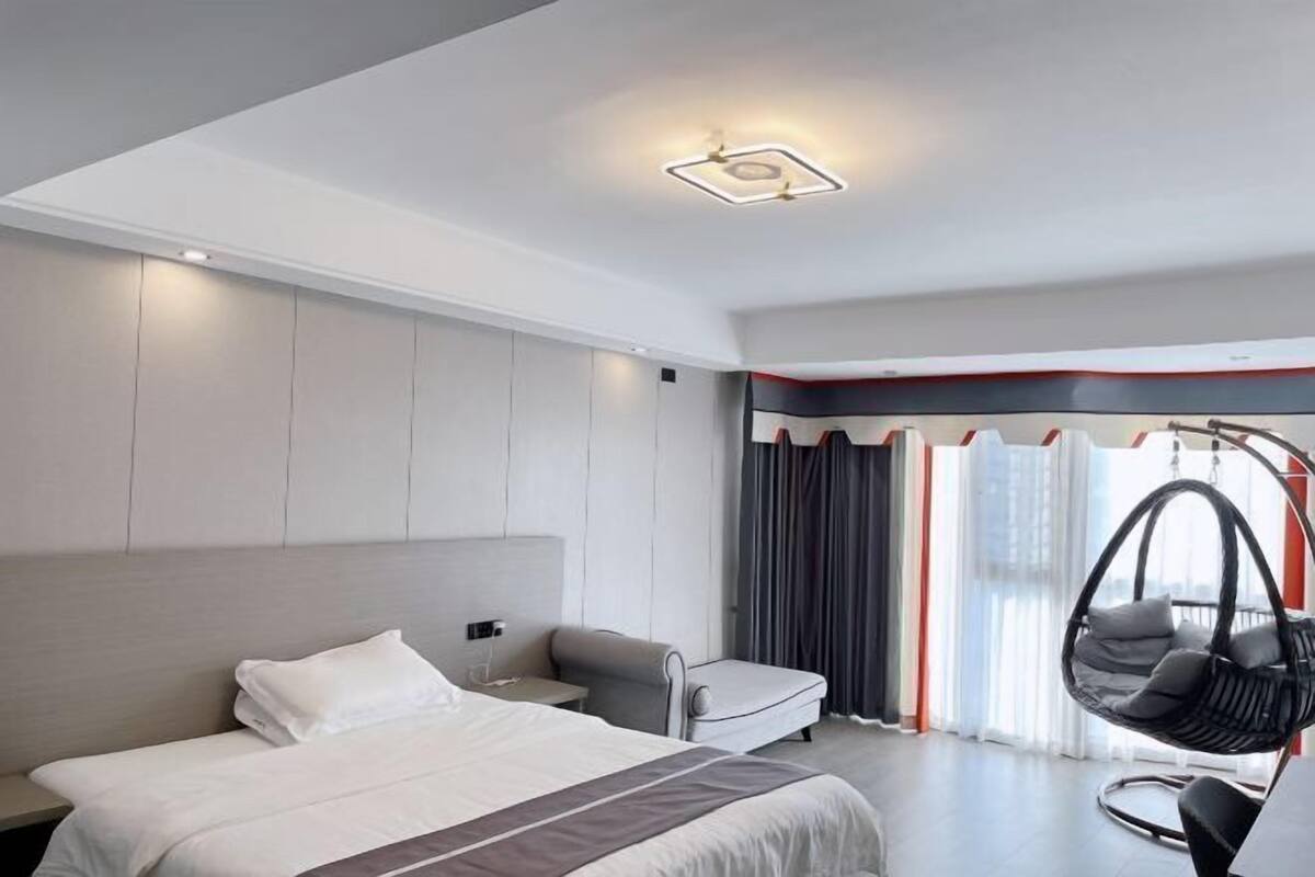 A modern hotel room with a large bed, a desk, a chair, and a hanging chair.