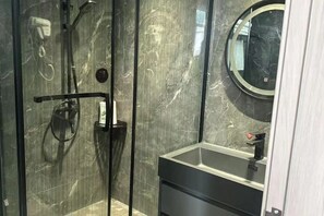 Un baño moderno con ducha envuelta en vidrio, un espejo redondo y un lavamanos minimalista.